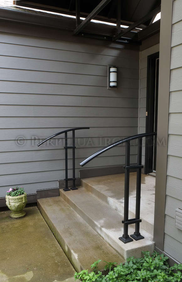  View of two modern hand rails. Two square vertical bars hold an assymetrical arc shaped handle works on two or three steps.  
